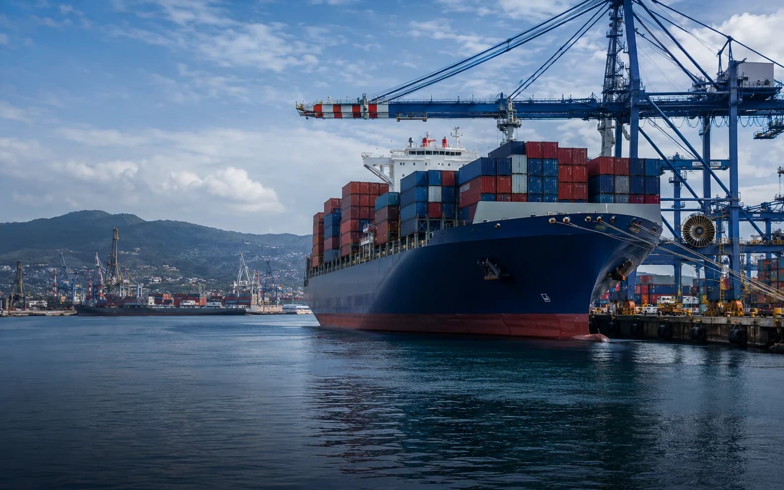 Loaded container vessel alongside port cranes